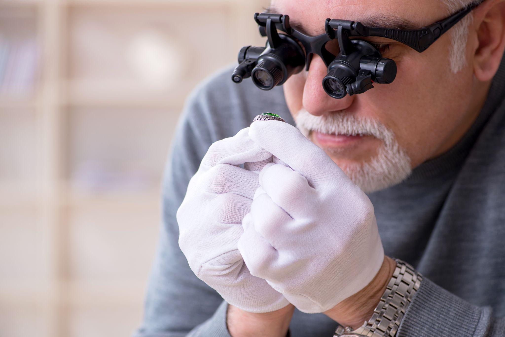 White bearded jeweler at workshop inspecting diamond.