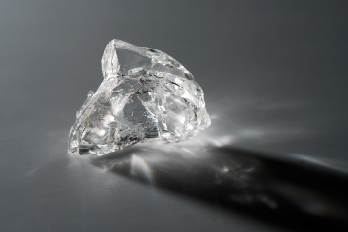 Single raw diamond on gray background.